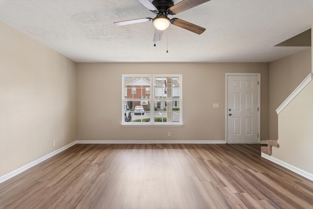unfurnished living room with baseboards, a textured ceiling, a ceiling fan, and wood finished floors