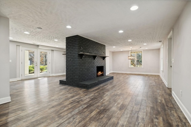 unfurnished living room with dark wood-type flooring, a textured ceiling, baseboards, and a brick fireplace