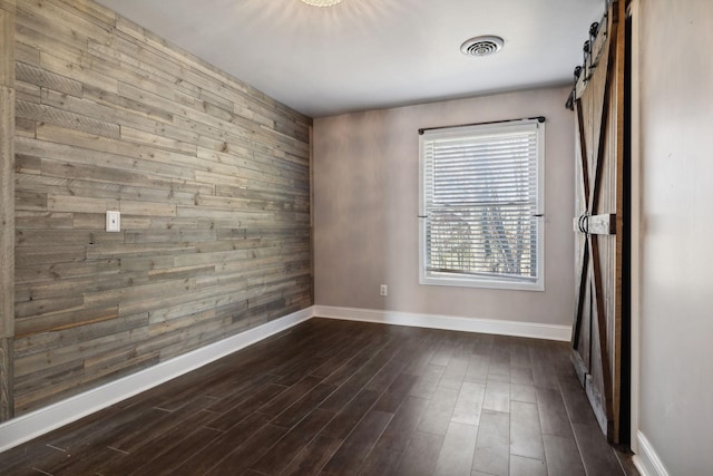spare room with a barn door, visible vents, baseboards, and dark wood-style floors