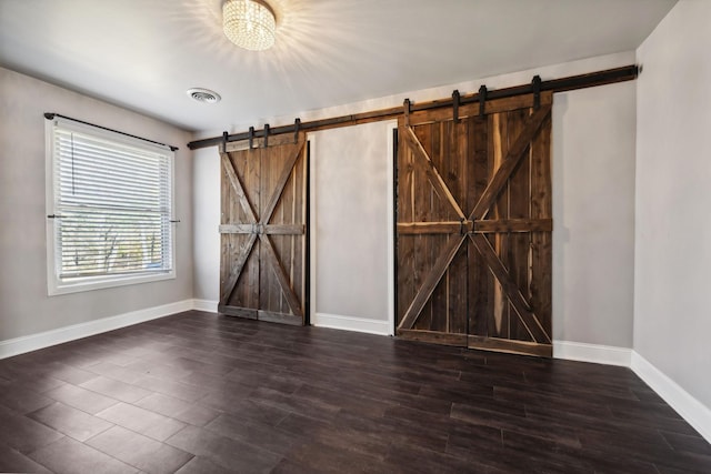 unfurnished room with visible vents, baseboards, a barn door, and wood finished floors