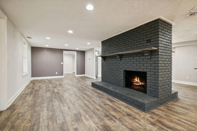 unfurnished living room featuring baseboards, a fireplace, a textured ceiling, visible vents, and wood finished floors