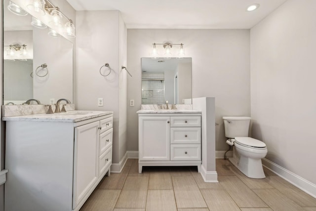 bathroom with a shower stall, two vanities, a sink, and baseboards