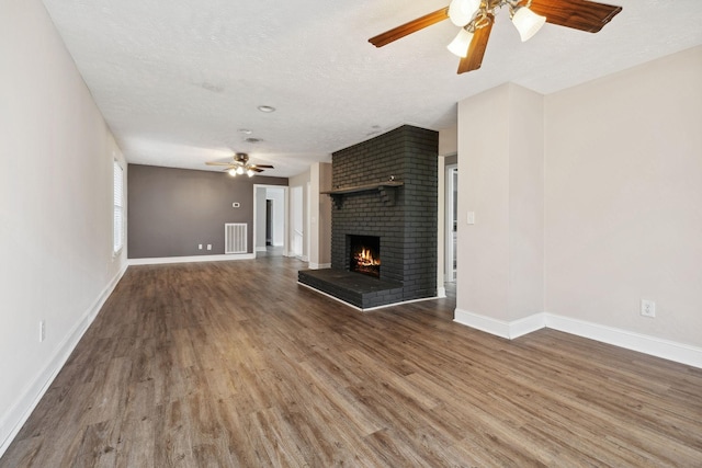 unfurnished living room featuring visible vents, a ceiling fan, a textured ceiling, a fireplace, and wood finished floors