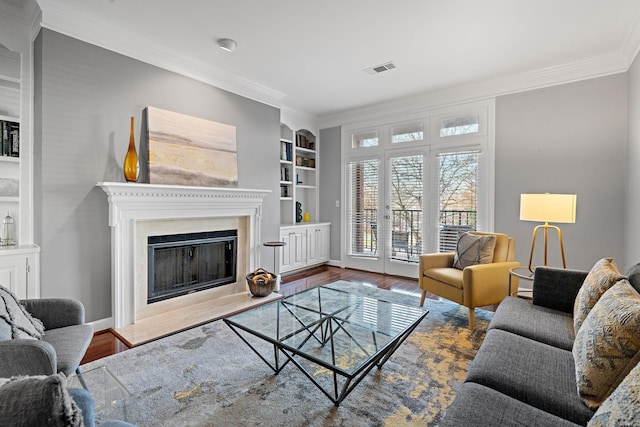 living area with built in features, a fireplace, ornamental molding, visible vents, and wood finished floors