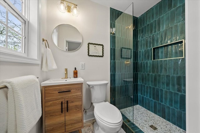 bathroom featuring toilet, tiled shower, and vanity
