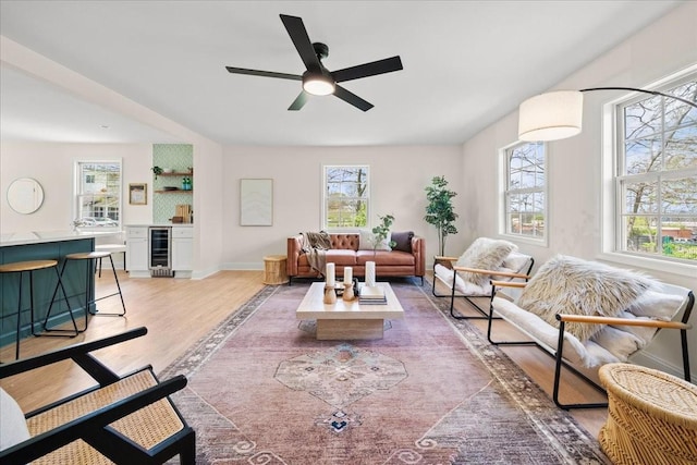 living area with light wood-type flooring, plenty of natural light, beverage cooler, and a ceiling fan