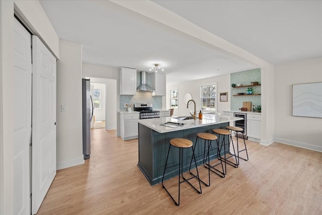 kitchen with wall chimney range hood, light wood finished floors, stainless steel appliances, backsplash, and beverage cooler