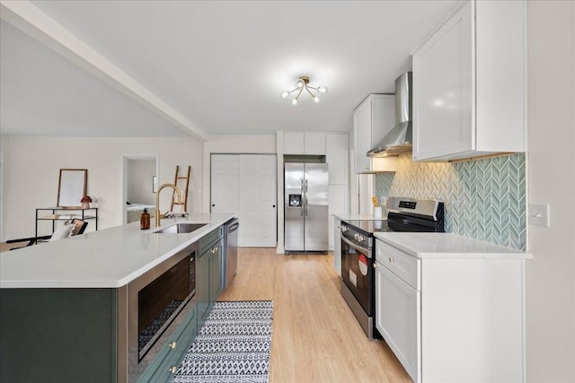 kitchen featuring light countertops, white cabinets, wall chimney exhaust hood, appliances with stainless steel finishes, and a sink