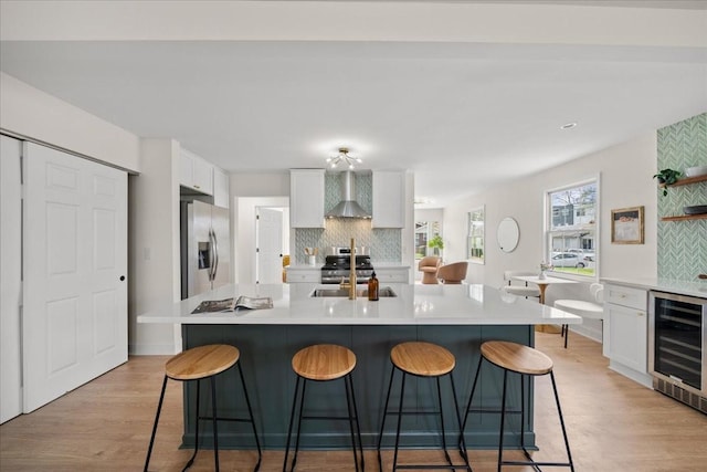 kitchen featuring wall chimney range hood, white cabinets, appliances with stainless steel finishes, wine cooler, and decorative backsplash