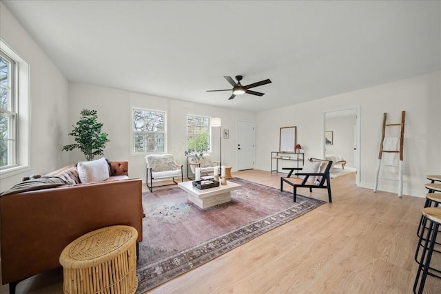 living area with light wood-style flooring, a ceiling fan, and baseboards