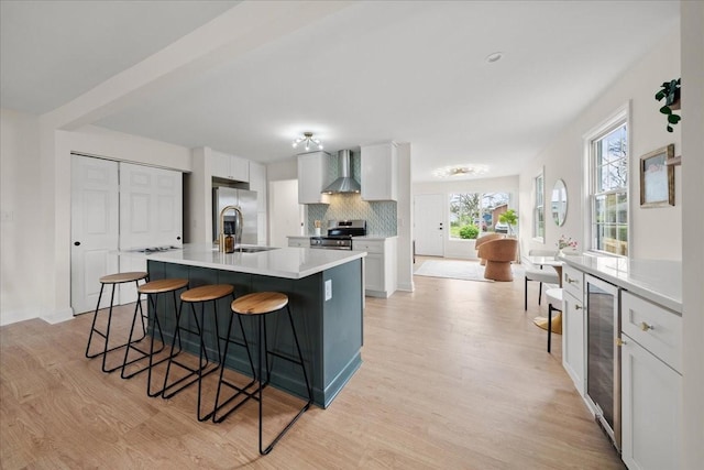 kitchen featuring stainless steel appliances, a kitchen breakfast bar, wall chimney exhaust hood, and beverage cooler