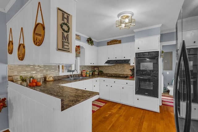 kitchen with a peninsula, crown molding, black appliances, range hood, and a sink