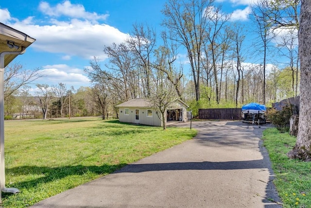 view of yard with aphalt driveway, fence, and an outdoor structure