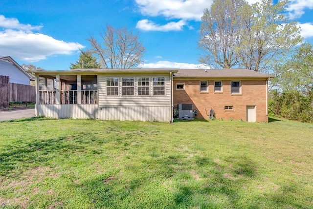 back of property featuring brick siding, a sunroom, and a lawn