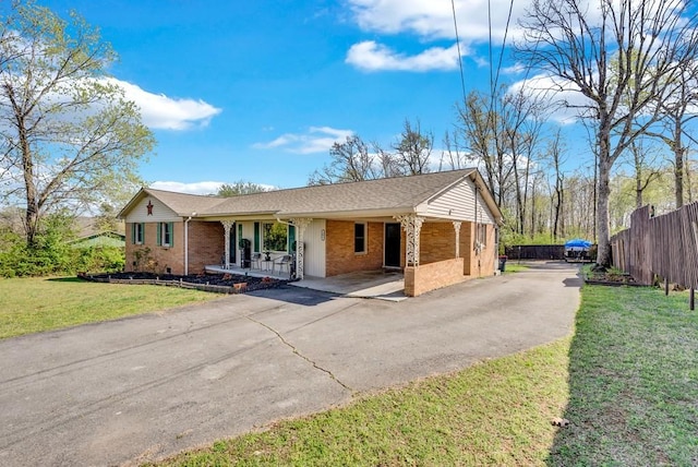 ranch-style home featuring a carport, aphalt driveway, fence, brick siding, and a front lawn