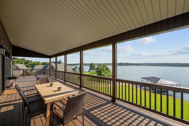 wooden terrace with a water view, outdoor dining space, and a lawn