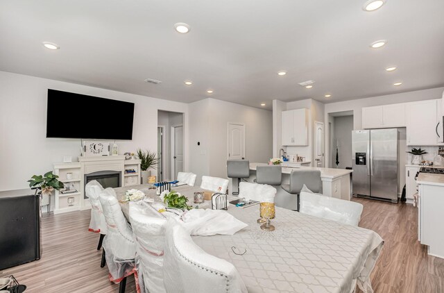 dining space with a glass covered fireplace, recessed lighting, light wood-style floors, and visible vents
