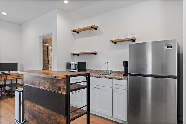 kitchen with open shelves, a sink, appliances with stainless steel finishes, white cabinetry, and light wood-style flooring