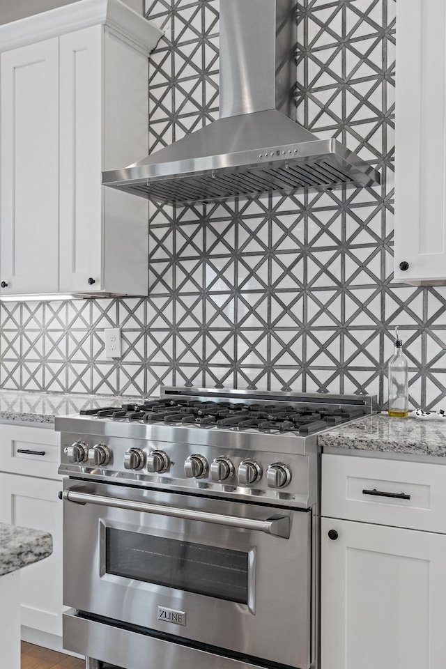 kitchen with decorative backsplash, stainless steel stove, wall chimney range hood, and white cabinets