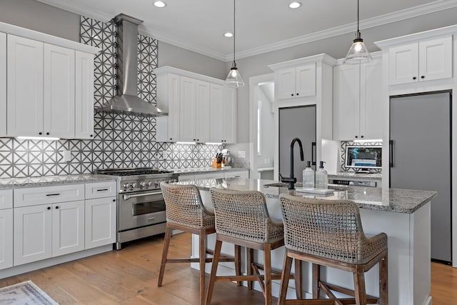 kitchen with wall chimney range hood, recessed lighting, a kitchen island with sink, and appliances with stainless steel finishes