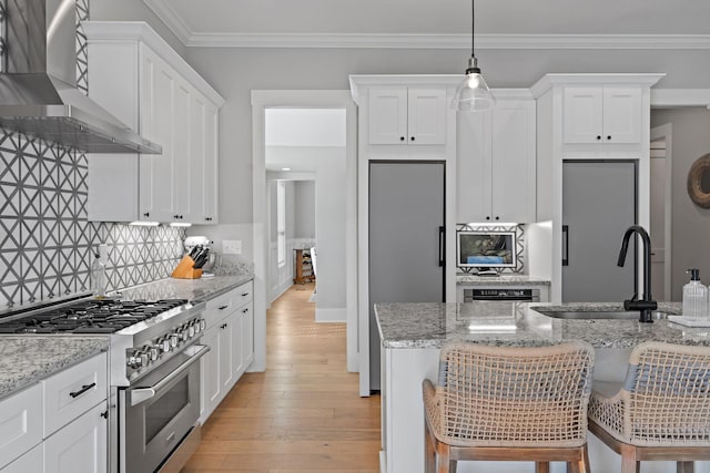 kitchen with high end stainless steel range, wall chimney exhaust hood, light wood-type flooring, white cabinetry, and a sink