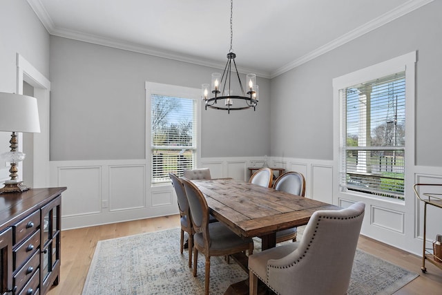 dining space featuring ornamental molding, light wood-style flooring, a chandelier, and wainscoting
