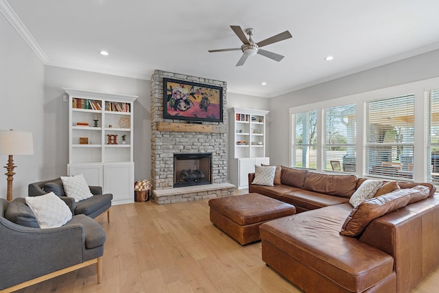 living area with ornamental molding, ceiling fan, a stone fireplace, recessed lighting, and light wood-style flooring