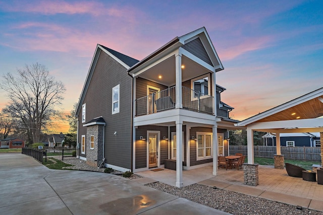 back of house at dusk with fence, a patio, and a balcony