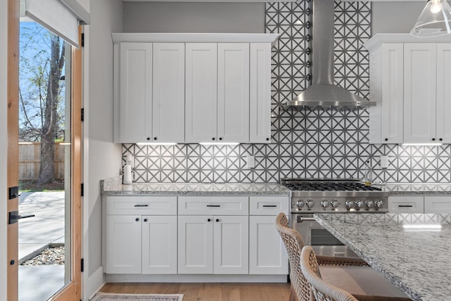 kitchen with white cabinets, decorative backsplash, wall chimney exhaust hood, and high end stove