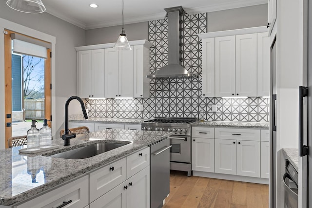 kitchen with a sink, wall chimney range hood, appliances with stainless steel finishes, and white cabinetry