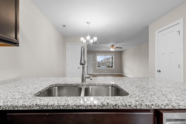 kitchen featuring dark brown cabinetry, light stone counters, open floor plan, ceiling fan, and a sink