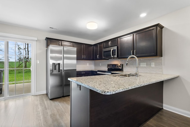 kitchen with visible vents, a peninsula, light wood finished floors, light stone countertops, and stainless steel appliances