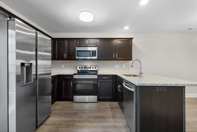 kitchen with a sink, a peninsula, dark wood-style floors, stainless steel appliances, and light stone counters