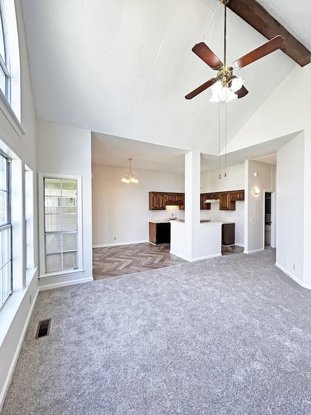 unfurnished living room with ceiling fan with notable chandelier, high vaulted ceiling, visible vents, carpet flooring, and baseboards