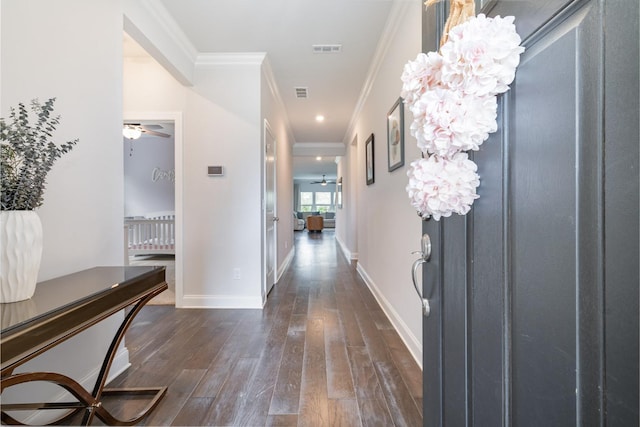 corridor with dark wood-type flooring, visible vents, baseboards, and crown molding
