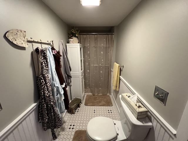 bathroom with a stall shower, wainscoting, and toilet