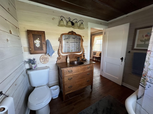 full bath with wood finished floors, wood walls, toilet, and vanity