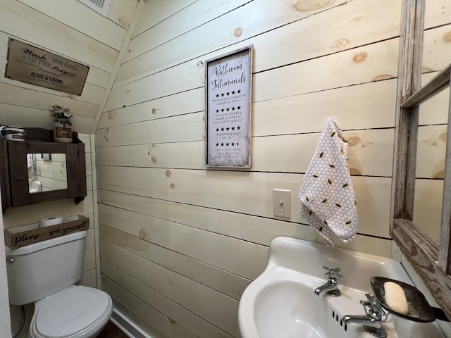 half bathroom with wood walls, toilet, and a sink
