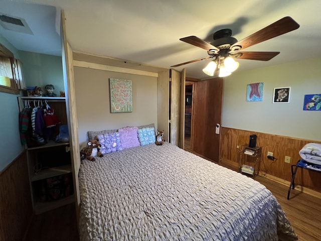 bedroom with wainscoting, wood finished floors, wooden walls, and ceiling fan