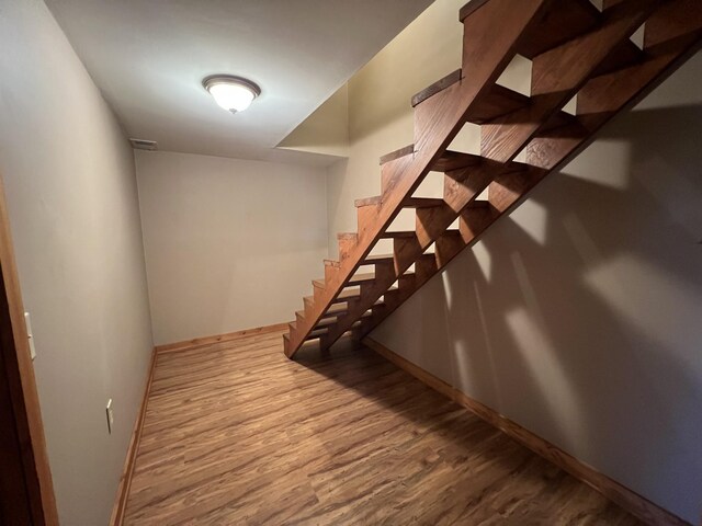 basement featuring wood finished floors, baseboards, and stairway
