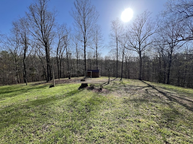 view of grassy yard with a view of trees and an outdoor structure