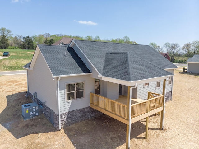 rear view of house with roof with shingles, stone siding, cooling unit, and a wooden deck