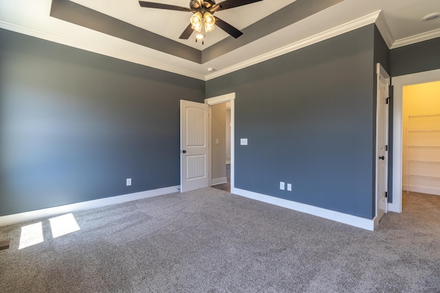 unfurnished room featuring a tray ceiling, a ceiling fan, ornamental molding, carpet floors, and baseboards