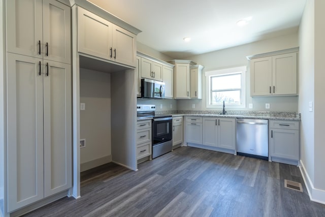 kitchen with baseboards, light stone counters, visible vents, dark wood finished floors, and stainless steel appliances