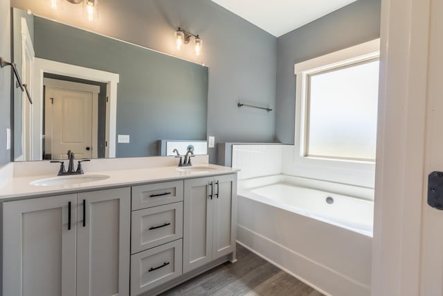 full bath with a sink, double vanity, wood finished floors, and a garden tub