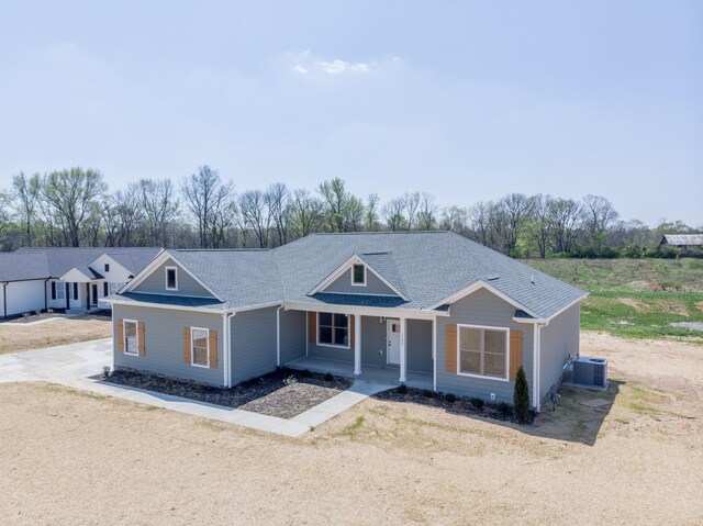 ranch-style house featuring central AC, dirt driveway, a porch, and a shingled roof