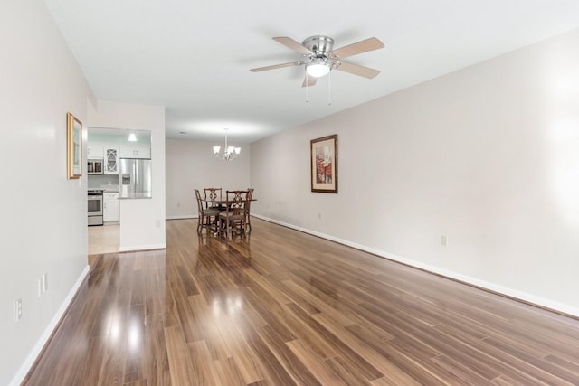 unfurnished living room with ceiling fan with notable chandelier, baseboards, and wood finished floors