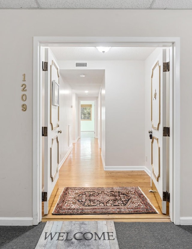 corridor featuring a drop ceiling, visible vents, baseboards, and light wood-style flooring