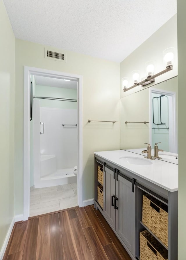 full bathroom featuring wood finish floors, a textured ceiling, visible vents, toilet, and walk in shower