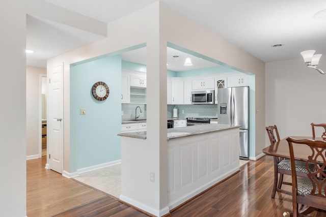 kitchen with stainless steel appliances, light wood-style flooring, white cabinetry, and backsplash